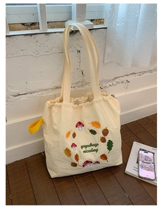 Close-up of mushroom and acorn embroidery on off-white nylon tote bag with drawstring