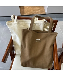 Detailed view of heavy canvas tote bags with YEYUBAG logo on a vintage wicker chair