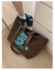 Detailed close-up of brown corduroy tote bag with blue embroidery and plaid lining