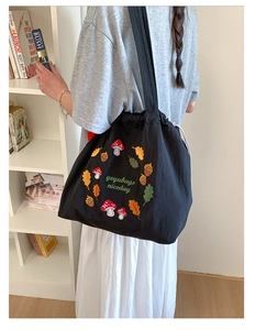Detail view of colorful mushroom embroidery and drawstring closure on a black tote bag