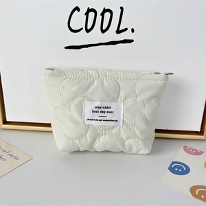 Detail of cream quilted cosmetic bag with floral stitching and branded woven label