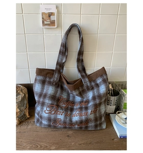 Close-up of brown plaid tote bag featuring corduroy trim and elegant script embroidery