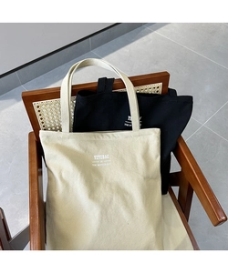 Close-up of beige and black canvas tote bags with YEYUBAG logo on a rattan chair