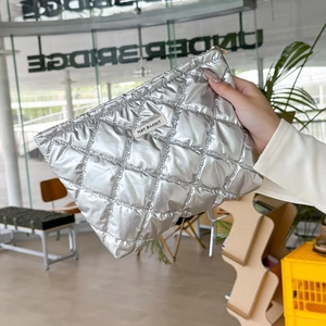 Close-up of silver quilted puffy pouch with gold zipper and brand tag in a cafe setting