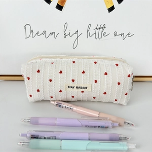 Detail of striped cream makeup bag featuring red heart embroidery and woven brand label