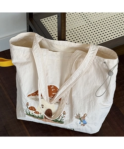 Detailed close-up of cream tote bag with embroidered mushroom house and rabbit design