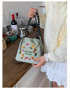 Detail of light green bucket bag with forest embroidery and woven rope handle on wood