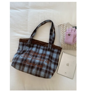 Close-up of plaid tweed tote bag with corduroy trim and embroidery on white fabric