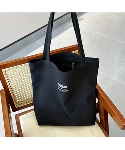 Detail of black canvas tote bag with metal zipper and white typography text on wooden chair