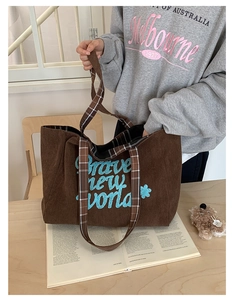 Close-up of brown corduroy tote bag with blue floral embroidery and plaid strap