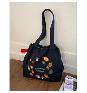 Close-up of mushroom embroidery and red strap detail on a black nylon tote bag