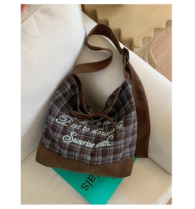 Detailed close-up of blue plaid canvas shoulder bag with brown corduroy trim on a sofa
