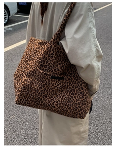 Outdoor view of a large leopard print tote bag with wide strap on a model's shoulder