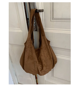 Brown suede hobo tote bag hanging on a white wooden door showing large capacity texture