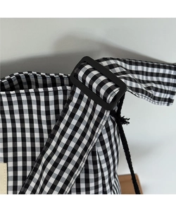 Detail of adjustable strap with black plastic buckle on gingham canvas tote bag