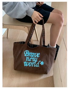 Detail of coffee corduroy tote with blue 'Brave new world' embroidery and plaid lining