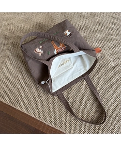 Detail of large brown canvas tote bag featuring forest animal embroidery and inner pocket
