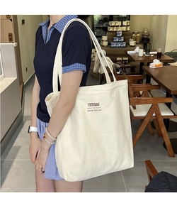 Lifestyle shot of an off-white canvas tote bag with shoulder straps and brown text print