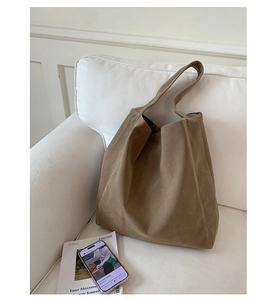 Detail shot of a brown wool tote bag on a white sofa with a magazine and a phone