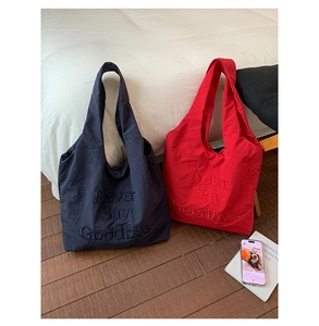 Detail of red and navy nylon tote bags with embossed Never Say Goodbye lettering