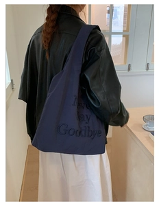 Navy nylon tote bag with 3D letter embroidery worn by a model in a minimal setting