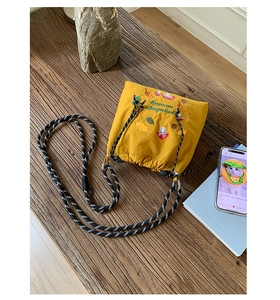 Detail of yellow nylon bag with mushroom embroidery and braided cotton rope strap