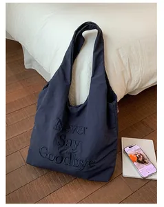 Detail of embroidered 'Never Say Goodbye' slogan on navy nylon tote bag surface
