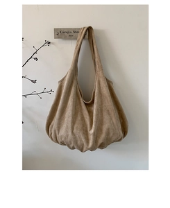 Detail of a large khaki suede tote bag with soft pleats hanging on a minimalist wall hook