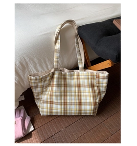 Detailed top view of a large plaid tote bag in yellow and brown canvas on a cozy white bed