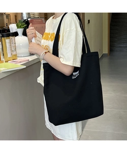 Side view of a large black canvas tote bag worn by a model in a casual cafe setting