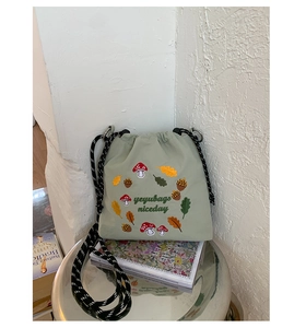 Close-up of green nylon crossbody bag featuring colorful mushroom embroidery and woven drawstring