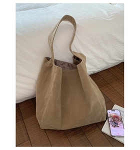 Detailed view of the large camel suede tote bag resting on a white minimalist bedsheet