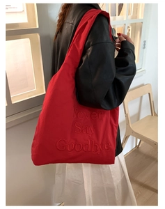 Detail of red nylon tote bag with 3D embroidery showing shoulder strap and draping