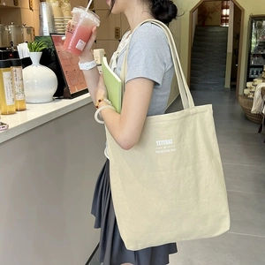 Minimalist beige canvas tote bag with lettering shown on model in a modern cafe setting