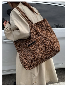 Close-up of leopard print tote bag with black woven label worn by model in outdoor setting