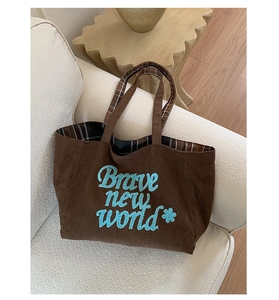 Detail of brown corduroy tote with Brave New World embroidery on a cozy sofa