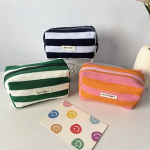 Three striped plush pencil cases with zippers and brand labels in a lifestyle setting