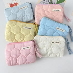 Détail de porte-monnaie en nylon matelassé aux couleurs pastel avec tirettes en corde