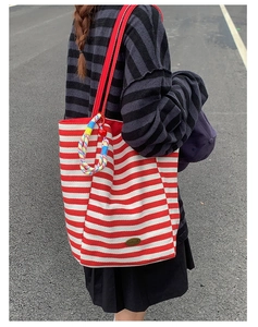 Detail of red and white striped canvas tote bag with woven charm and metal handmade tag