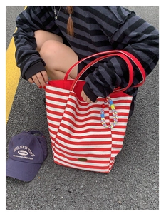 Detailed view of striped canvas tote bag with woven charm and metal logo emblem