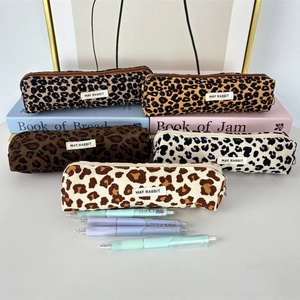 Various leopard print corduroy pencil cases stacked on books with stationery items