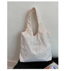 Detailed embroidery of Never Say Goodbye text on minimalist white nylon tote bag