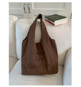 Detailed close-up of brown nylon tote bag featuring Never Say Goodbye embroidery