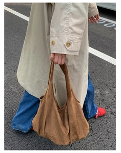Outdoor shot of a brown suede tote bag held by a model in a beige trench coat