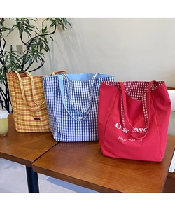 Three large canvas tote bags in red, blue and yellow plaid on a wooden table