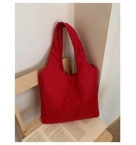 Detail view of a red nylon tote bag featuring 3D letter embroidery on a wooden chair