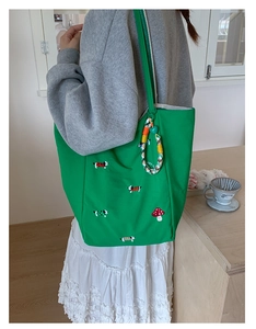 Detail of green canvas tote featuring mushroom and puppy embroidery with striped straps