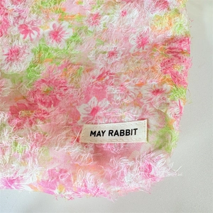 Detail of floral makeup bag featuring plush fringe texture and a woven May Rabbit label