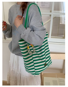 Detail of green and white striped canvas tote bag with woven charm and metal logo patch