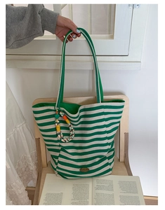 Detail of green and white striped canvas tote with embroidered mushroom and woven charm